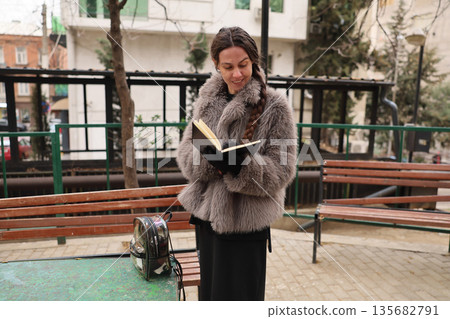 Reading quietly in a cozy urban park on a chilly afternoon, wrapped in soft fur for warmth Reading quietly in a cozy urban park on a chilly afternoon, wrapped in soft fur for warmth 135682791