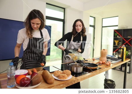 Cooking together in a bright kitchen as two friends prepare a delicious meal with fresh ingredients 135682805