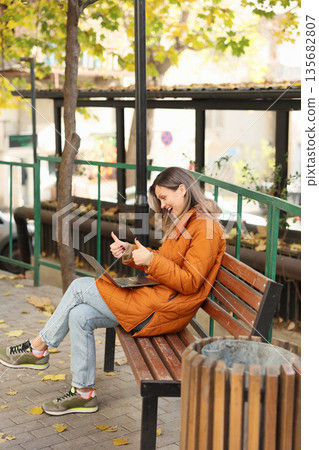 Enjoying a sunny afternoon working on a laptop in a park surrounded by autumn leaves 135682807