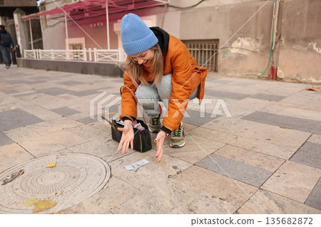 Young woman excitedly discovers money on the street during a sunny day in a vibrant city Young woman excitedly discovers money on the street during a sunny day in a vibrant city 135682872