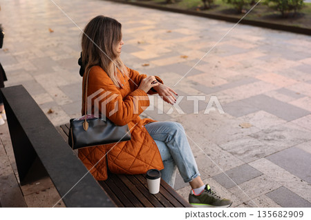 Watching the time while sipping coffee in an autumn park setting Watching the time while sipping coffee in an autumn park setting 135682909