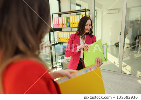 Busy professionals organize colorful files in a bright, modern office environment filled with natural light 135682930
