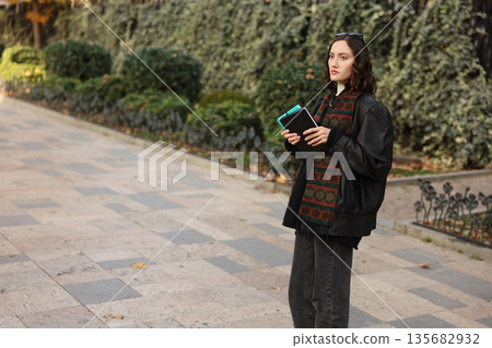 Woman holding notebooks and enjoying a serene stroll in a lush garden during the golden afternoon light 135682932