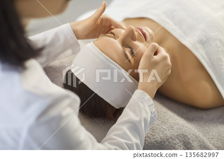 Esthetician performing gentle facial massage on woman resting at calm spa Esthetician performing gentle facial massage on woman resting at calm spa 135682997