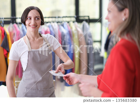 Friendly shop assistant handing over a receipt to a happy customer in a bright clothing store Friendly shop assistant handing over a receipt to a happy customer in a bright clothing store 135683380