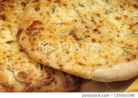 Two pieces of flatbread topped with melted cheese and herbs are placed on a wooden board in a kitchen during the afternoon 135683396