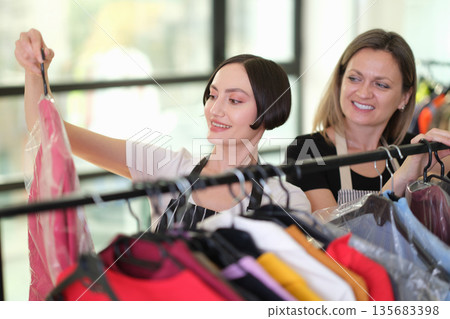 Women enjoy shopping for colorful clothing at a vibrant boutique on a sunny afternoon Women enjoy shopping for colorful clothing at a vibrant boutique on a sunny afternoon 135683398