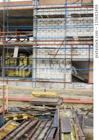 Workers are engaged in building a structure with scaffolding and various materials at a construction site. The scene shows ongoing construction activity 135683404