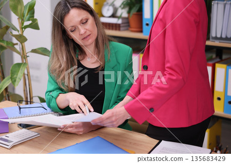 Two colleagues collaborate at a bright office workspace, sharing documents and ideas during a productive afternoon meeting 135683429