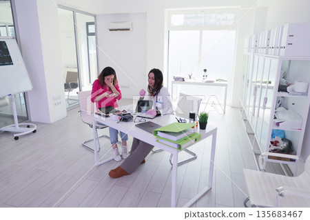 Women engaged in a lively discussion in a modern office environment during daylight hours 135683467