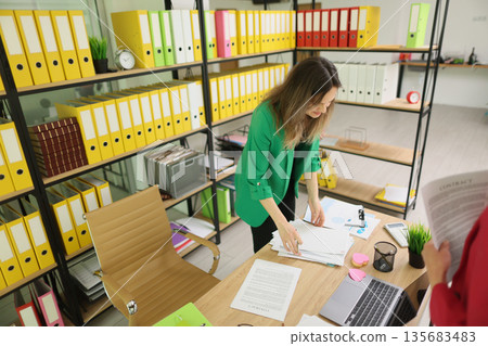 Office scene showing a woman organizing paperwork amidst vibrant colored folders during a productive workday Office scene showing a woman organizing paperwork amidst vibrant colored folders during a productive workday 135683483