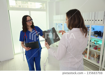 Exciting collaboration between two healthcare professionals discussing patient X-ray in a modern clinic setting 135683708