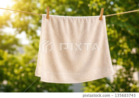 White Towel Hanging on Clothesline Outdoors in Sunny Green Garden 135683743