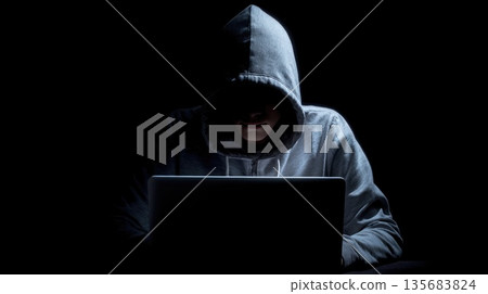 Hooded Person Using Laptop in Dark Environment 135683824