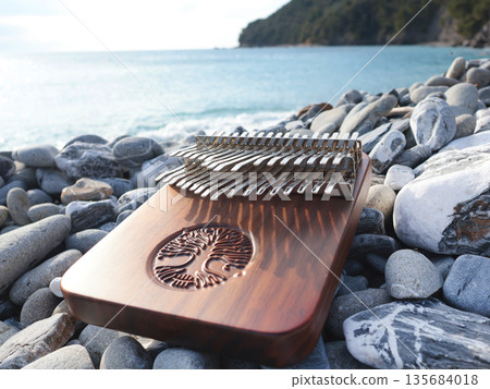 Kalimba musical instrument on stones by sea. Nature near mountains, music, and meditation. Relaxation and mental health.  135684018