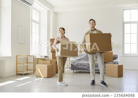 Happy couple carrying cardboard boxes while moving into new apartment together 135684098