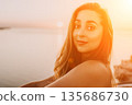 Woman Sunset Portrait featuring a beautiful young lady smiling near the ocean during golden hour at sunrise for travel and lifestyle concepts 135686730
