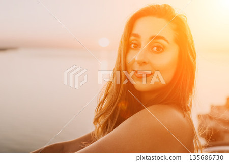 Woman Sunset Portrait featuring a beautiful young lady smiling near the ocean during golden hour at sunrise for travel and lifestyle concepts 135686730