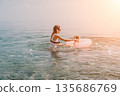 Mother daughter sea playing with a pink inflatable ring in the calm water at sunset for summer vacation happiness 135686769