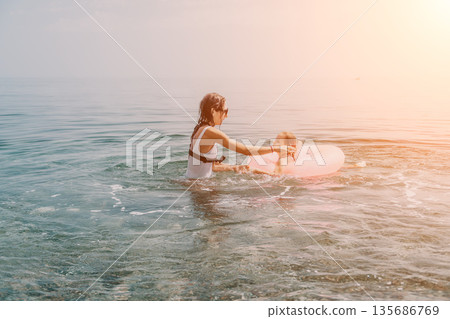 Mother daughter sea playing with a pink inflatable ring in the calm water at sunset for summer vacation happiness 135686769