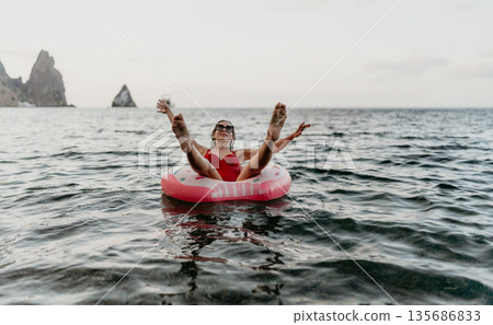 Woman swimsuit vacation happy woman floats on inflatable donut ring in ocean near cliffs on summer holiday Woman swimsuit vacation happy woman floats on inflatable donut ring in ocean near cliffs on summer holiday 135686833