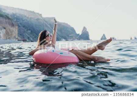 Woman Ocean Float Happy woman relaxing on a pink donut float in the calm sea near scenic cliffs. 135686834