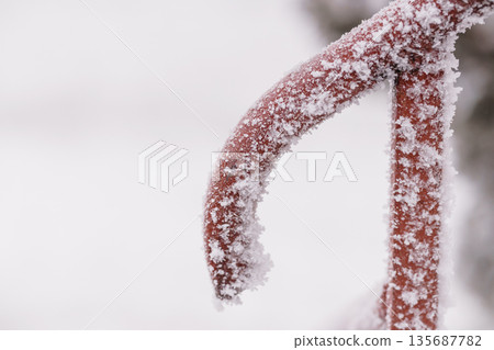 Frost-covered red metal railing in snowy winter landscape with icy textures and soft white background Frost-covered red metal railing in snowy winter landscape with icy textures and soft white background 135687782