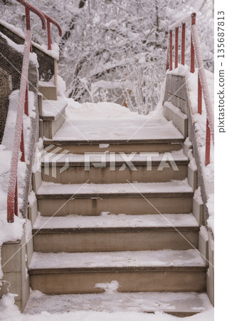 Snow-Covered Stone Staircase with Red Railings Surrounded by Frozen Trees in a Winter Landscape Snow-Covered Stone Staircase with Red Railings Surrounded by Frozen Trees in a Winter Landscape 135687813