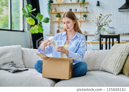 Young happy woman unpacking cardboard box with online order 135688181