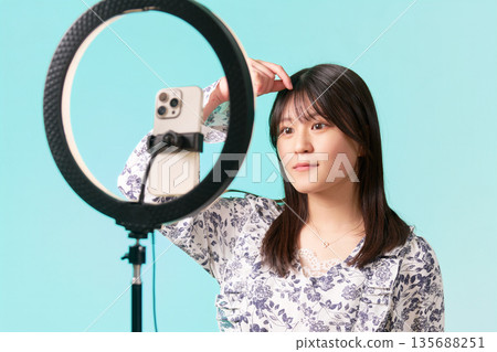 A female influencer adjusts her bangs while preparing for a live stream in front of a ring light A female influencer adjusts her bangs while preparing for a live stream in front of a ring light 135688251