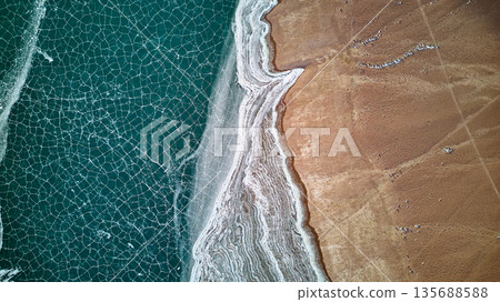 Aerial view of cracked ice on lake with frozen shore and brown land Aerial view of cracked ice on lake with frozen shore and brown land 135688588