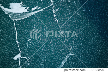 Abstract aerial top down view of cracked ice on dark blue lake water. Abstract aerial top down view of cracked ice on dark blue lake water. 135688589