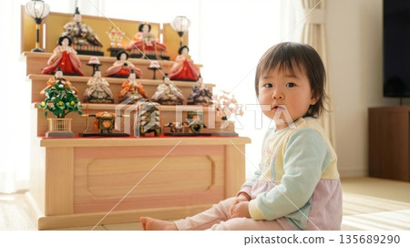 A cute girl sits in front of a natural wooden Hina doll displayed in the living room 135689290