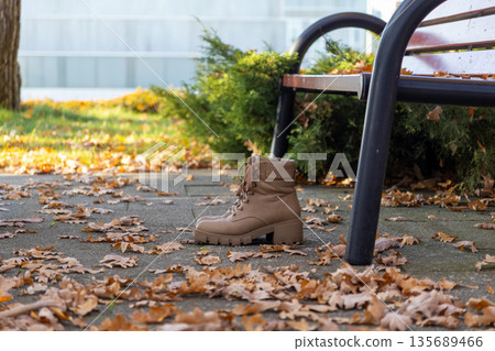 Stylish brown combat boots with laces placed on a concrete path amidst vibrant fallen autumn leaves, evoking cozy fall fashion and outdoor walks Stylish brown combat boots with laces placed on a concrete path amidst vibrant fallen autumn leaves, evoking cozy fall fashion and outdoor walks 135689466