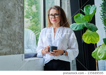 Portrait of middle aged beautiful woman with cup, near window 135689595