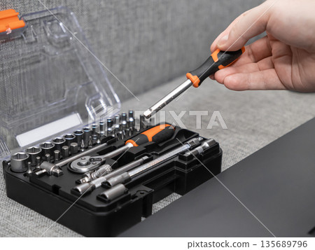 Hand taking an orange and black screwdriver from a comprehensive mechanic tool kit for essential home repair, professional maintenance, or DIY projects Hand taking an orange and black screwdriver from a comprehensive mechanic tool kit for essential home repair, professional maintenance, or DIY projects 135689796