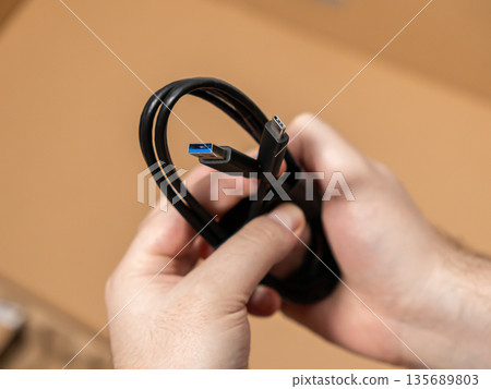 Human hands holding a black USB cable, showcasing both modern Type-A and Type-C connectors for universal device connectivity and efficient data transfer Human hands holding a black USB cable, showcasing both modern Type-A and Type-C connectors for universal device connectivity and efficient data transfer 135689803