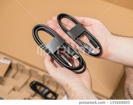 Hands holding two new black USB cables, one Type-A to Type-C and one Type-C to Type-C, for modern device connectivity and consumer electronics Hands holding two new black USB cables, one Type-A to Type-C and one Type-C to Type-C, for modern device connectivity and consumer electronics 135689805