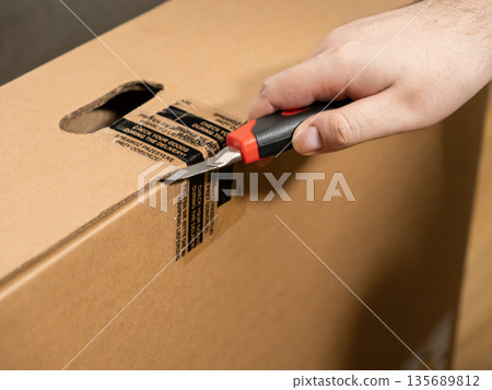 Customer hand opening a large brown cardboard shipping box with a utility knife, highlighting the importance of inspecting new goods upon delivery Customer hand opening a large brown cardboard shipping box with a utility knife, highlighting the importance of inspecting new goods upon delivery 135689812