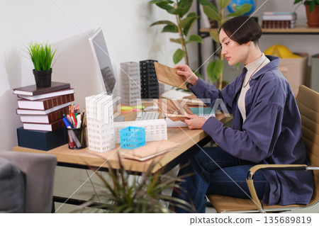 Creative designer analyzing building materials in a modern workspace filled with plants and books 135689819