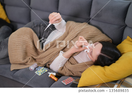 Cozy afternoon spent battling a cold while bundled in a warm blanket on a gray sofa 135689835