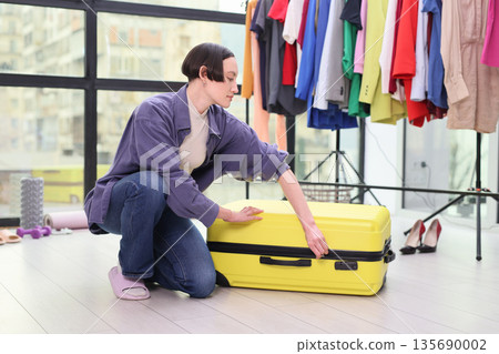 Packing a bright yellow suitcase in a stylish room filled with colorful clothes and fashion items 135690002