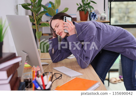 Busy professional experiencing a challenging moment at her home office desk while on an important phone call Busy professional experiencing a challenging moment at her home office desk while on an important phone call 135690042