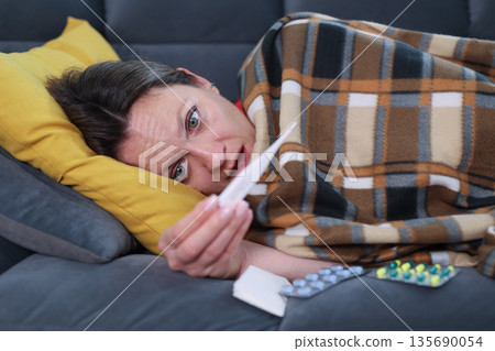 Feeling unwell while resting on the couch with a blanket and medication during a cold winter afternoon Feeling unwell while resting on the couch with a blanket and medication during a cold winter afternoon 135690054