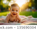 Happy baby crawls on picnic blanket in green park with sunset light behind; baby smile is bright and joyful as baby scene reflects warmth innocence and family love 135690304