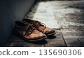 Old brown leather shoes rest by wall on grey pavement; shoes look used and wrinkled as leather shoes show signs of age and wear in urban outdoor scene 135690306
