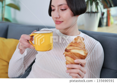 Enjoying a cozy morning with coffee and a fresh croissant in a stylish living room Enjoying a cozy morning with coffee and a fresh croissant in a stylish living room 135690591