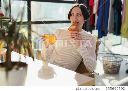 Enjoying a warm croissant and golden coffee in a stylish, sunlit caf during a cozy morning break Enjoying a warm croissant and golden coffee in a stylish, sunlit caf during a cozy morning break 135690592