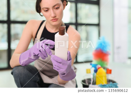 Woman in gloves examines cleaning product in a modern, bright interior after a thorough cleaning session Woman in gloves examines cleaning product in a modern, bright interior after a thorough cleaning session 135690612