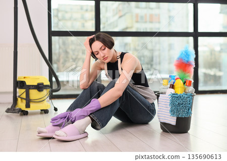 Feeling overwhelmed while cleaning a modern living space in the afternoon light with colorful supplies nearby 135690613